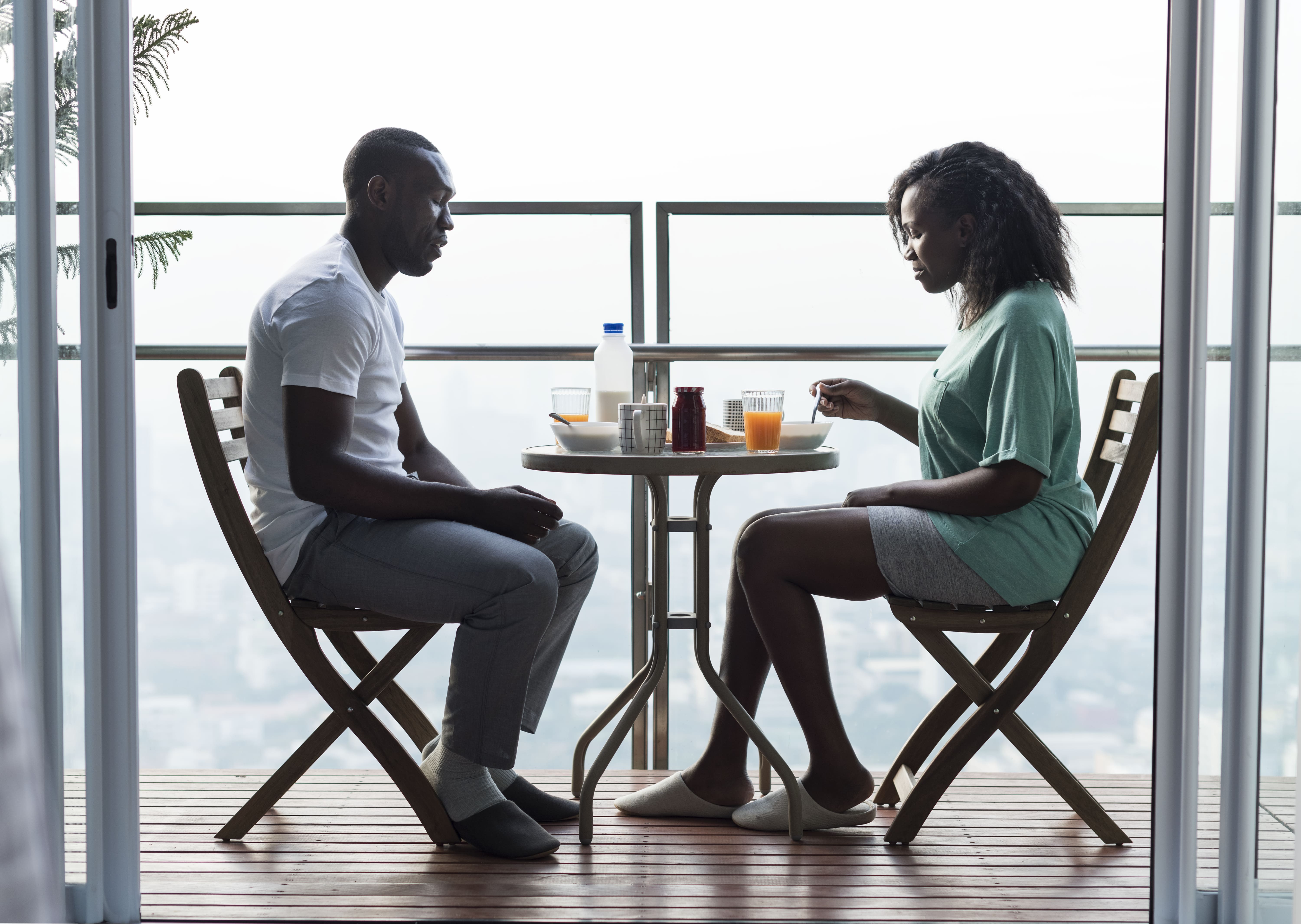 Two adults sharing a table while appearing emotionally present in different conversations.